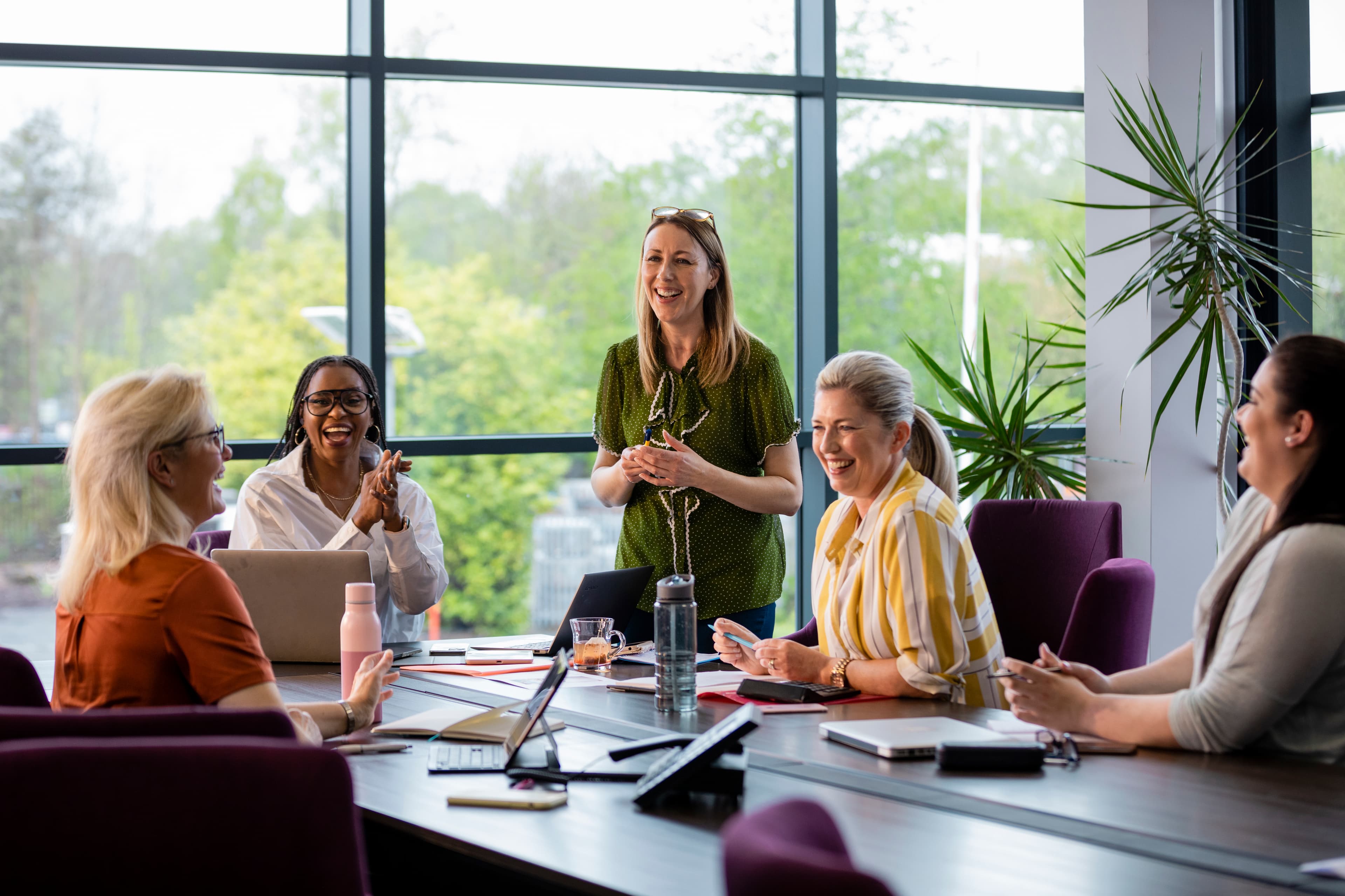 A group of women in a business casual environment smile and laugh.